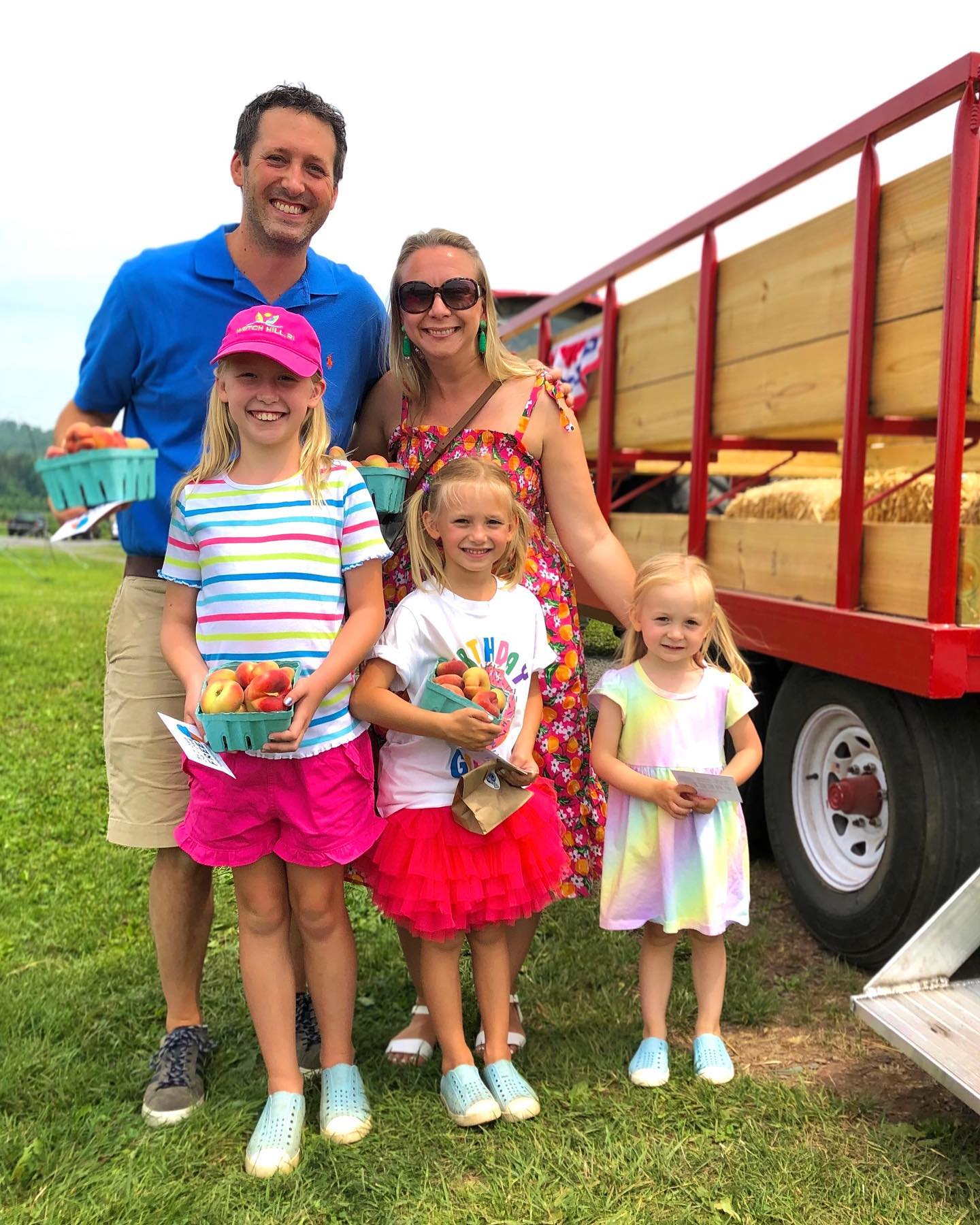 Family with three daughters enjoying cartons of nectarines next to a red truck